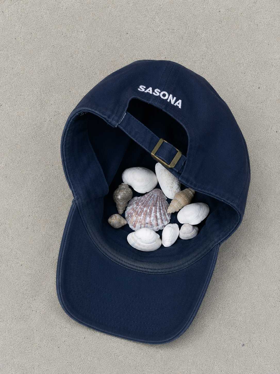 Dunkelblaue SASONA Cap mit Muscheln gefüllten am Strand im Urlaub